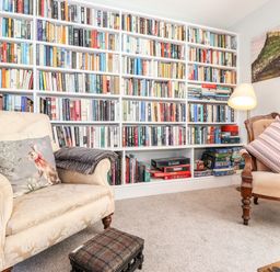 A reading room with a large bookshelf filled with books two armchairs a lamp and a small footstool at West Farm Cottage in Longhorsley