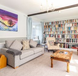 A living room with a gray sofa a wooden coffee table a bookshelf filled with books and an armchair at West Farm Cottage in Longhorsley