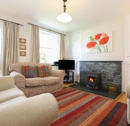 A living room with a fireplace armchairs a TV and a striped rug at High Stile in Seatoller near Rosthwaite