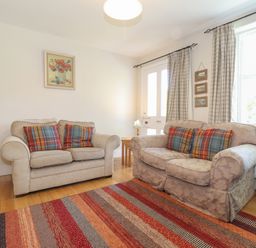 A living room with two sofas with plaid cushions a striped rug wooden door and window with curtains at High Stile in Seatoller near Rosthwaite