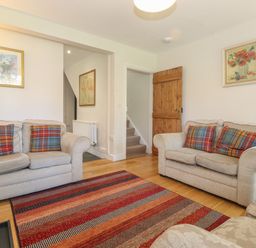 A living room with two beige sofas with plaid cushions a striped rug and wooden door at High Stile in Seatoller near Rosthwaite