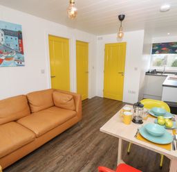 A living room with a brown sofa three yellow doors a dining table set with blue dishes and yellow mugs and a kitchen area visible at Nanny's Little House in Sandown