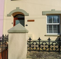 The exterior of a house with a red door window with shutters and black metal fence at Stones Throw in Tenby