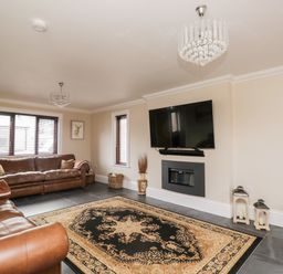 A living room with leather sofas a patterned rug a wall mounted tv and two chandeliers at Mill End in Eamont Bridge near Penrith