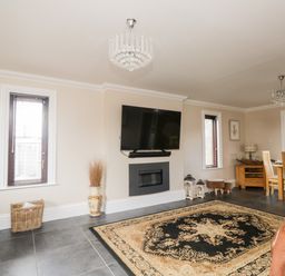 A living room with a wall-mounted TV a fireplace a patterned rug and a dining table with chairs at Mill End in Eamont Bridge near Penrith