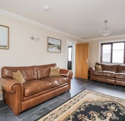 A living room with two brown leather sofas a wooden side table paintings on the wall and a patterned rug on a tiled floor at Mill End in Eamont Bridge near Penrith