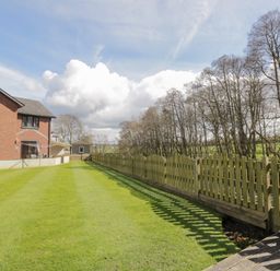 A backyard with a green lawn and a wooden fence next to a brick house at Mill End in Eamont Bridge near Penrith