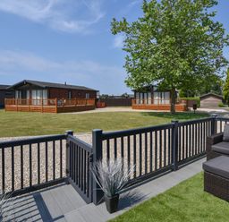 A fenced patio area with a chair and ottoman overlooking wooden lodges and a tree at Oakwood 2 Pinewood Retreat in Pinewood