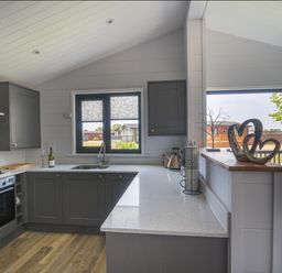 A kitchen with dark cabinets a countertop a sink stove and oven with a window and open doors at Oakwood 2 @ Pinewood Retreat in Pinewood