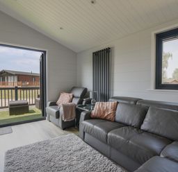 A living room with gray leather sofas, a gray armchair, a side table with a lamp, a rug, and an open door leading to a patio at Oakwood 2 @ Pinewood Retreat in Pinewood