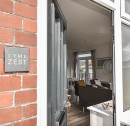 An open door showing a living room with chairs a table and curtains at Lyme Zest in Lyme Regis