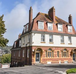A large brick and stucco building with multiple chimneys and black doors on a street corner at Lyme Zest in Lyme Regis