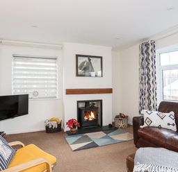 A living room with a fireplace a yellow chair a brown leather sofa and a wall-mounted television at Neaudd Wen in Red Wharf Bay near Benllech