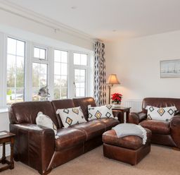 A sitting room with brown leather sofas a lamp and a window with patterned curtains at Neaudd Wen Red Wharf Bay near Benllech