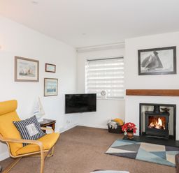 A living room with a yellow armchair a fireplace a TV and framed pictures on the wall at Neaudd Wen in Red Wharf Bay near Benllech