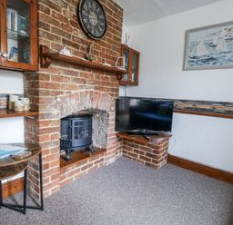 A living room with a brick fireplace and television at Saddlers Cottage in Weymouth