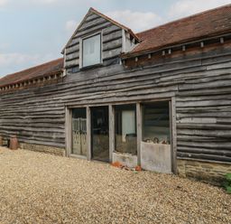 An exterior view of a wooden barn with gravel ground and small windows at Brandeers Long Barn in Brandier near Minety