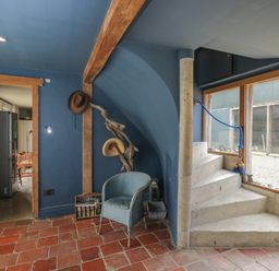A corner with a blue wicker chair hats hanging on a branch and stone spiral stairs next to a window at Brandeers Long Barn Brandier near Minety