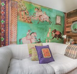 A room with a white sofa with colorful pillows a wooden wall a wall painting showing people on horses and an elephant and a round mirror at The Big Box Brandeers Brandier near Minety