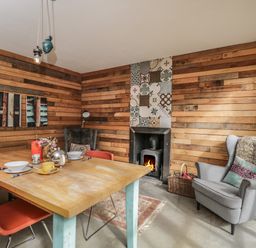 A dining room with a wooden table set for two red chairs a fireplace with patterned tiles and two gray armchairs at The Big Box Brandeers Brandier near Minety