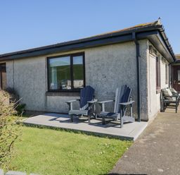 A small patio with two black chairs next to a grey house with a window and a door at Seaspray in St Bees