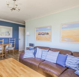 A living room with a brown leather sofa and striped cushions a wooden coffee table and dining table with chairs at Seaspray in St Bees