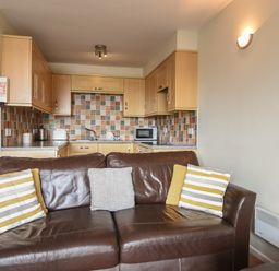 A kitchen with wooden cabinets and tiled backsplash behind a brown leather sofa with four pillows at 3 Bay View Court in Lyme Regis