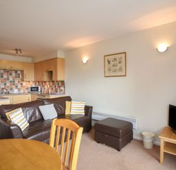 A living area with a brown leather sofa and pillows next to a kitchen with wooden cabinets and tiled backsplash at 3 Bay View Court in Lyme Regis