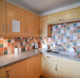A kitchen with wooden cabinets a tiled backsplash a sink a kettle and a toaster at 3 Bay View Court Lyme Regis