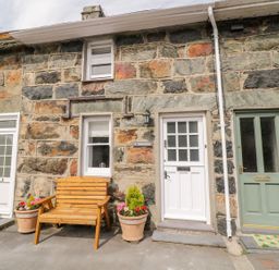 A stone exterior of a house with three doors two flower pots and a wooden bench at Henfro in Beddgelert