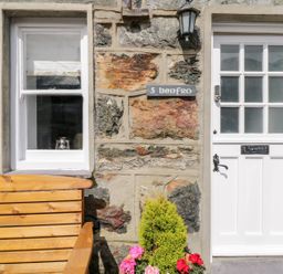 A stone wall with a white door and window a wooden bench and flowers at Henfro in Beddgelert