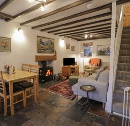 A living room with a dining table with four chairs a wood burning stove a TV an armchair a sofa a carpet and stairs with a baby gate at Henfro in Beddgelert