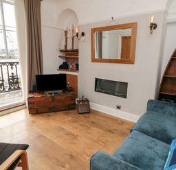 A living room with a television on a wooden chest a blue sofa and a triangular wooden shelf at The Seahome in Scarborough