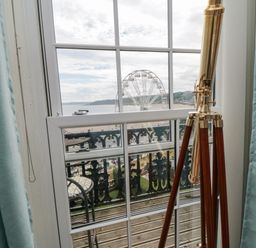 A telescope on a tripod in front of a window with a view of a Ferris wheel and beach at The Seahome in Scarborough