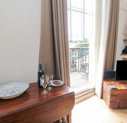 A room with a wooden table holding a bottle of wine two glasses and a plate of biscuits near a window with curtains and a wooden chest with a television at The Seahome in Scarborough