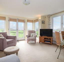 A living room with armchairs television and a dining table with chairs at Chase View Bowland Bridge near Bowness-On-Windermere