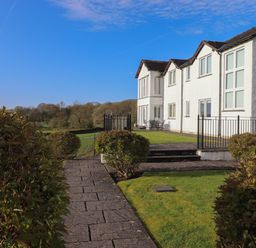 A pathway lined with bushes leading to a white building with multiple windows and outdoor seating at Chase View in Bowland Bridge near Bowness-On-Windermere