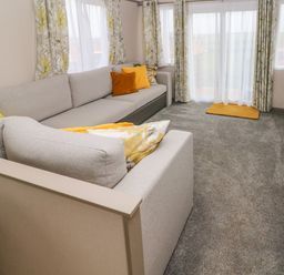 A living room with a large grey sectional sofa yellow cushions curtains and a carpet at The Waves in Little Haven near Broad Haven