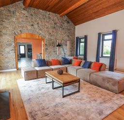 A living room with a large sectional sofa with blue and orange cushions a wooden coffee table and a stone wall at Heritage in St Clears