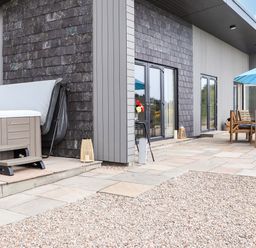 An outdoor patio area with a hot tub and wooden dining table with chairs under a blue umbrella at Pine Marten in Dornoch