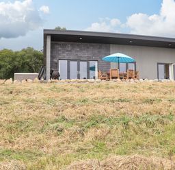 A modern house with outdoor furniture and an umbrella on a patio surrounded by a stone border at Pine Marten in Dornoch