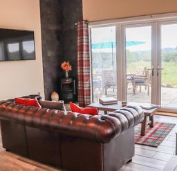 A living room with a leather sofa a wall-mounted tv a coffee table and glass doors opening to a patio at Pine Marten in Dornoch