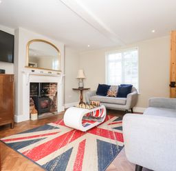 A living room with a fireplace a wall-mounted TV two sofas and a rug with a Union Jack design at Cavan Cottage in Yoxford