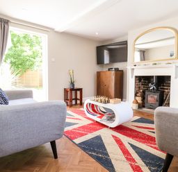 A living room with two gray armchairs a white coffee table with chess and other games a Union Jack rug a fireplace a wall-mounted TV and a small plant at Cavan Cottage in Yoxford