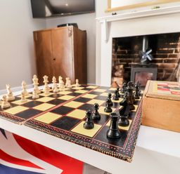 A chessboard with chess pieces set up on a table in a room with a fireplace and wooden furniture at Cavan Cottage in Yoxford