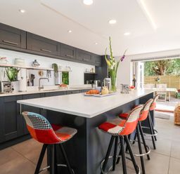 A kitchen with a large island and four stools and an open door leading to an outdoor dining area at Cavan Cottage in Yoxford