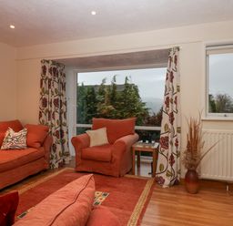 A sitting room with orange sofas and armchair a wooden side table and patterned curtains at Fairfield View in Ambleside