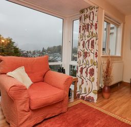 A living room with an orange armchair a floral curtain a wooden floor and a television at Fairfield View in Ambleside