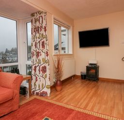 A corner of a living room with an orange armchair a floral curtain a wall-mounted television and a small stove at Fairfield View in Ambleside