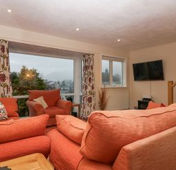 A living room with orange sofas a wall-mounted television and patterned curtains at Fairfield View in Ambleside